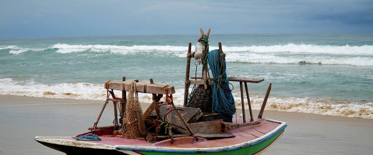 A small boat with a colorful hull on a sandy beach, with the ocean in the background.