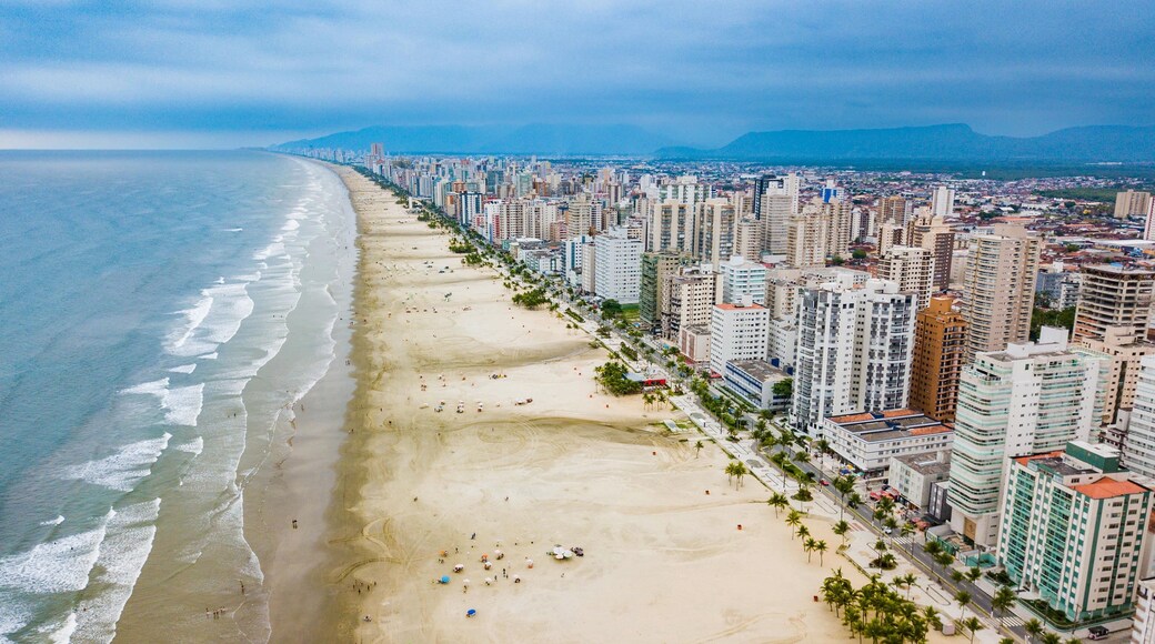 A coastal cityscape with a wide beach, high-rise buildings, and a distant mountain range.