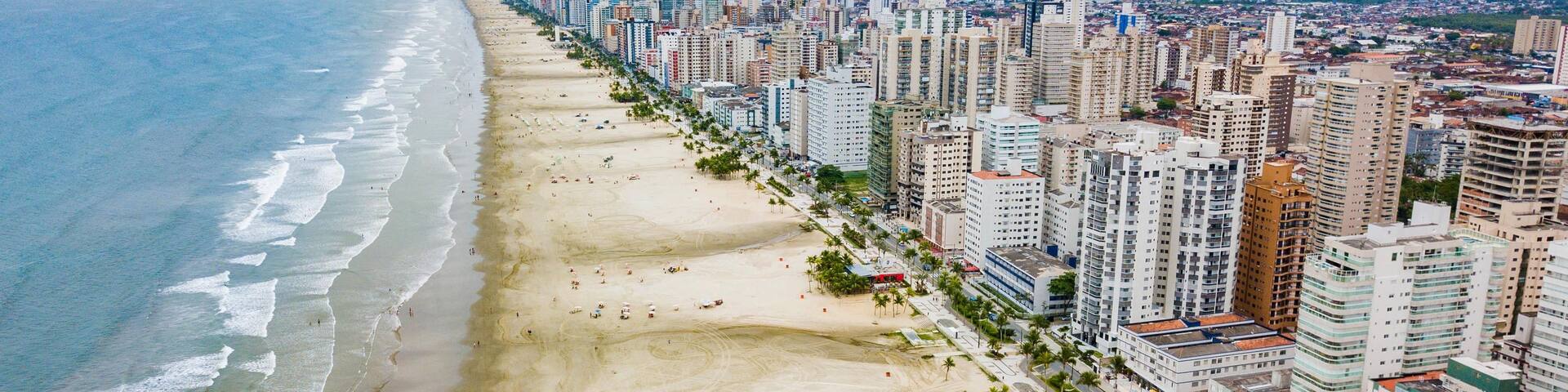 A coastal cityscape with a wide beach, high-rise buildings, and a distant mountain range.