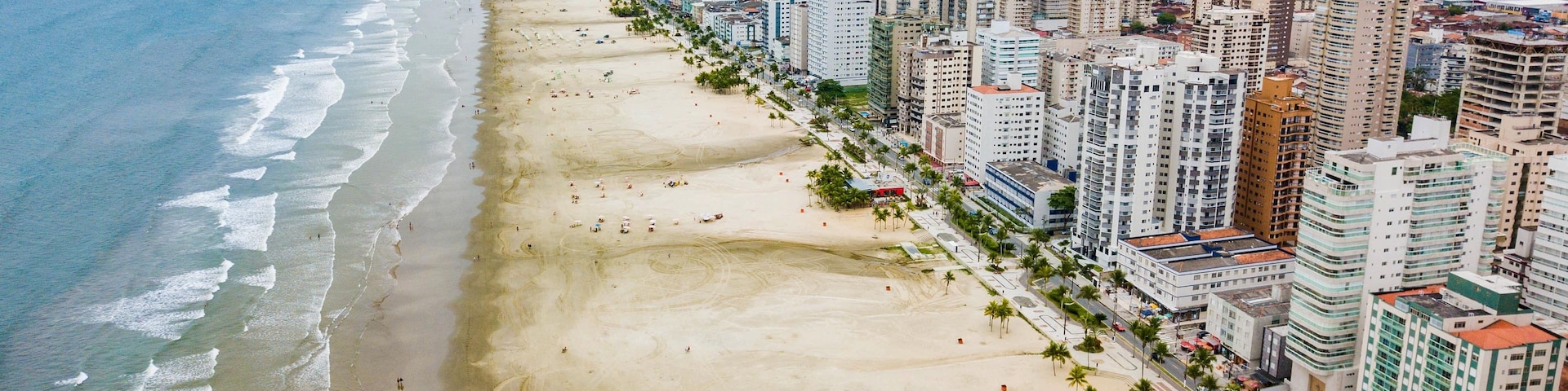 Paisagem costeira com uma extensa praia, edifícios altos e uma cadeia de montanhas ao longe.