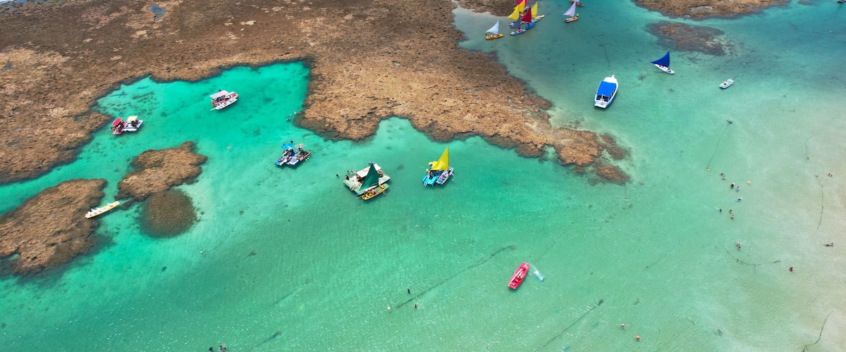 Een kustgebied met helder turquoise water, rotsachtige uitstulpingen en verschillende kleine boten en jachten.