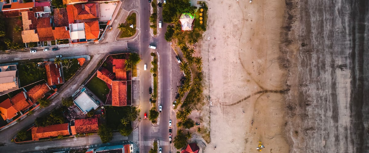 Vista aérea de un pueblo costero con edificios de techo rojo, una playa y una carretera.