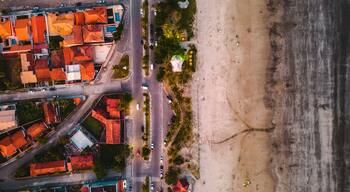 An aerial view of a coastal town with red-roofed buildings, a beach, and a road.