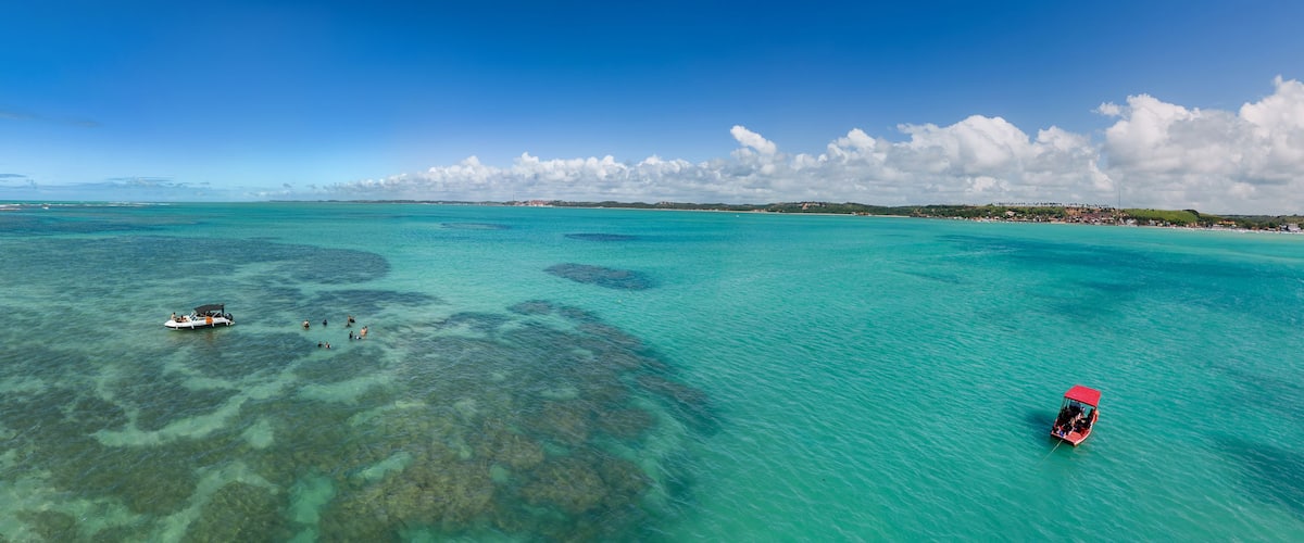 A turquoise sea with clear waters, a small boat, and a red boat on the right.