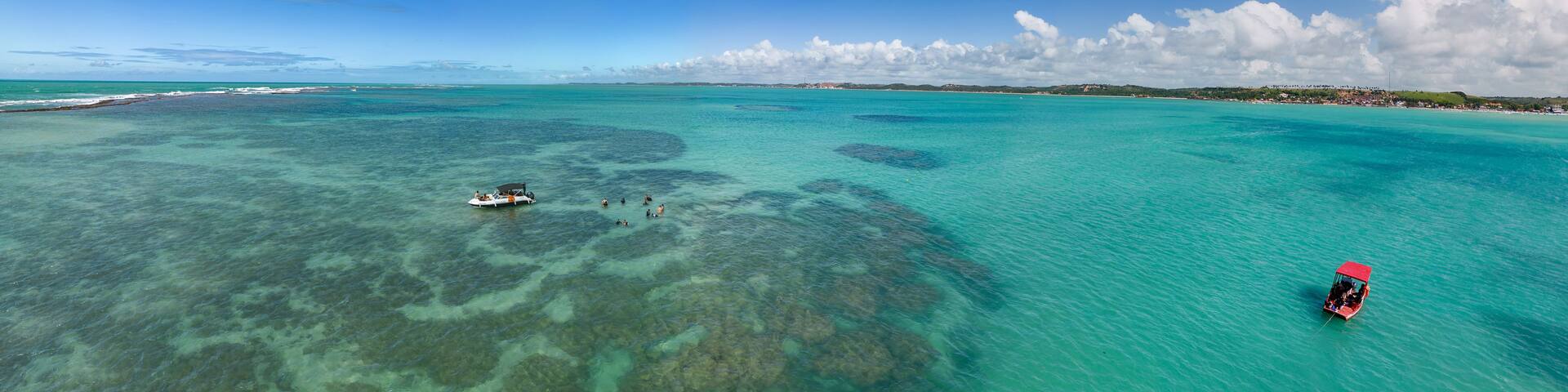 A turquoise sea with clear waters, a small boat, and a red boat on the right.