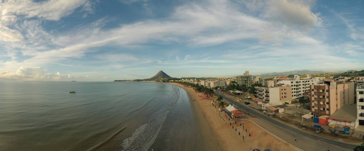 Paisagem costeira com praia, edifícios e montanhas ao longe.