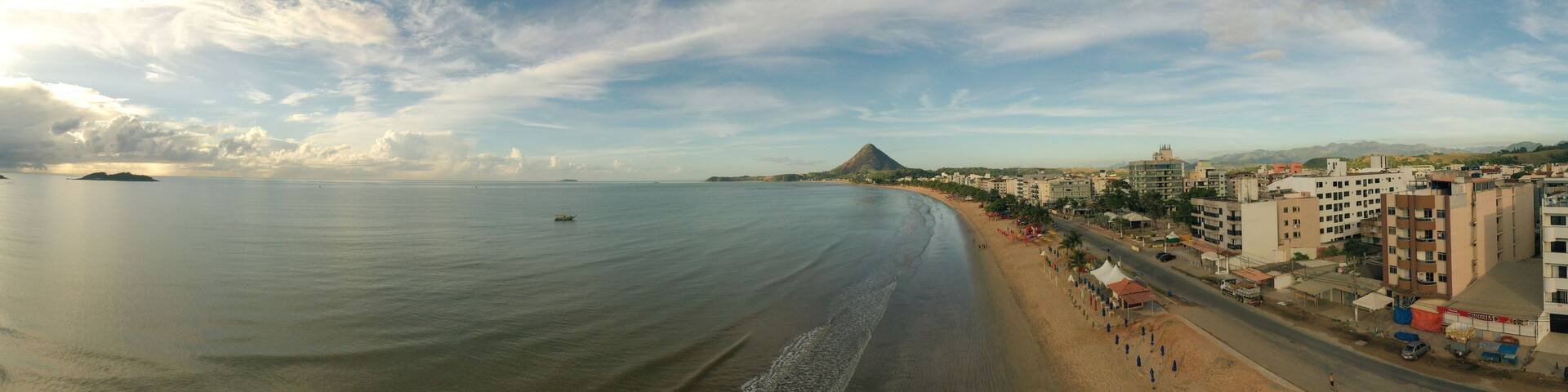 A coastal cityscape with a beach, buildings, and a mountain in the distance.