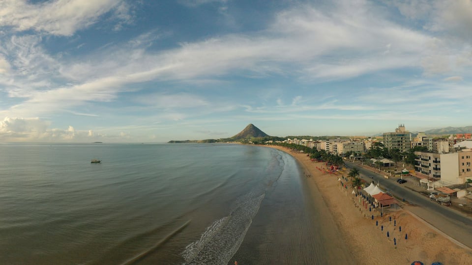 A coastal cityscape with a beach, buildings, and a mountain in the distance.