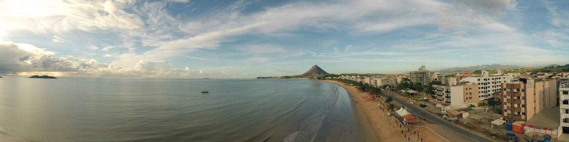 Paisagem costeira com praia, edifícios e montanhas ao longe.