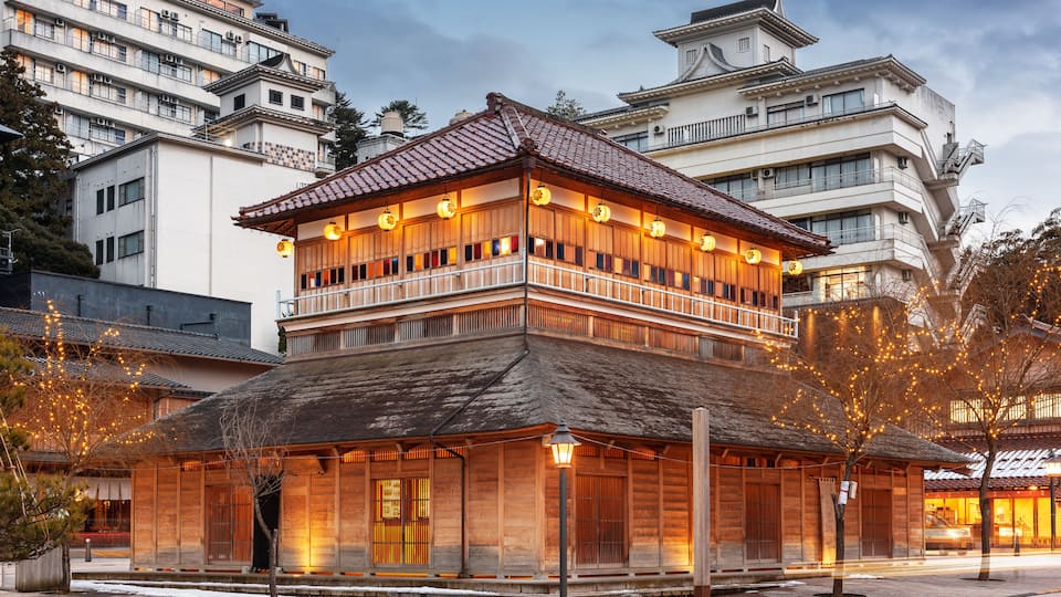 Un edificio tradicional de madera con techo de tejas, rodeado por modernos rascacielos.