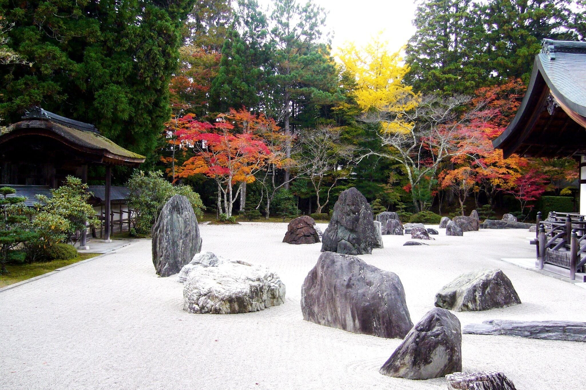 Un jardín japonés tradicional con rocas grandes, un pabellón de madera y árboles de tonos otoñales.