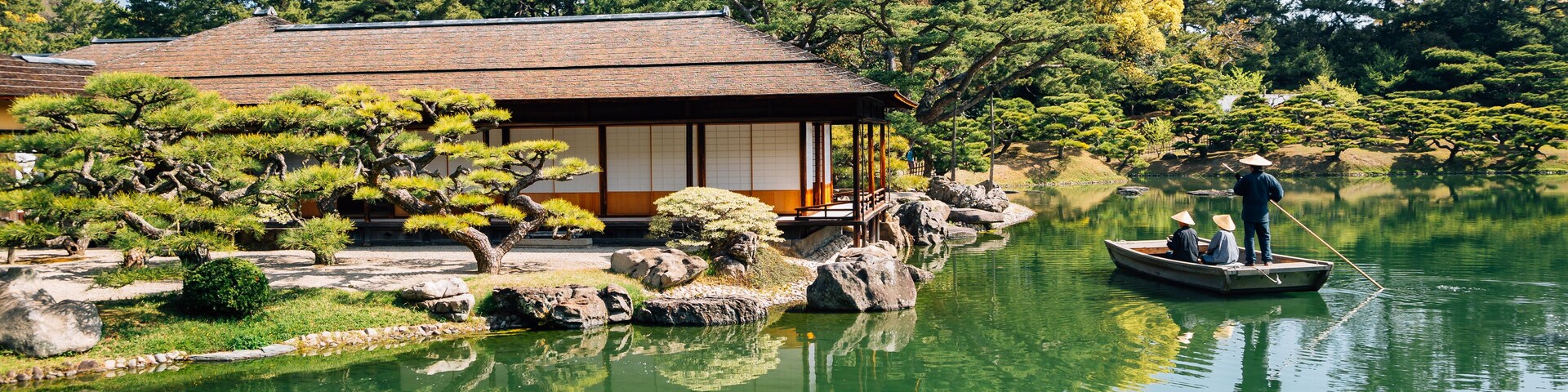 Un edificio japonés tradicional junto a un estanque tranquilo con una persona remando en un bote.
