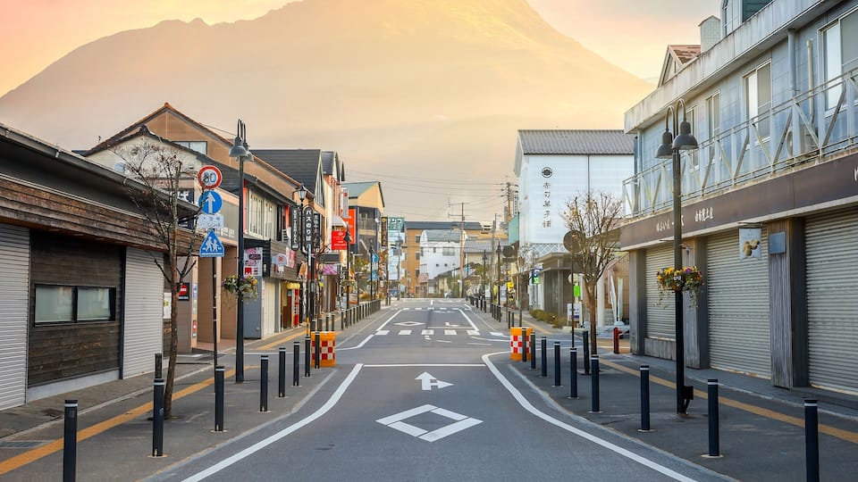 Une rue bordée d’immeubles, une montagne en arrière-plan et un ciel dégagé.
