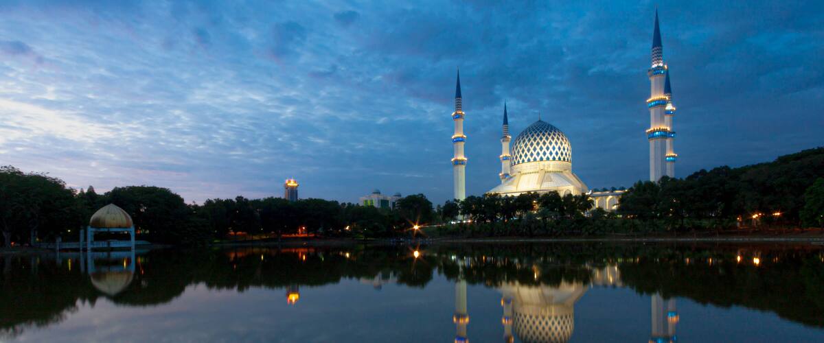 A mosque with a large dome and two minarets, reflecting in a calm body of water.