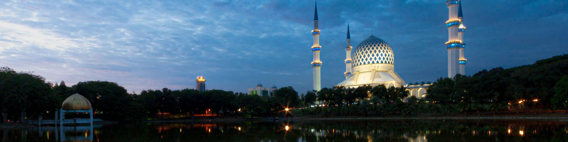 A mosque with a large dome and two minarets, reflecting in a calm body of water.