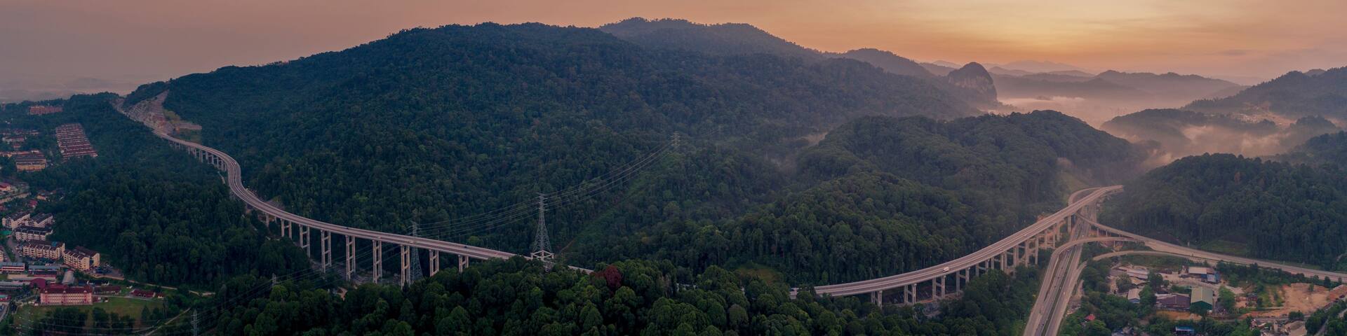 A long bridge curving through a mountainous landscape with dense forests.