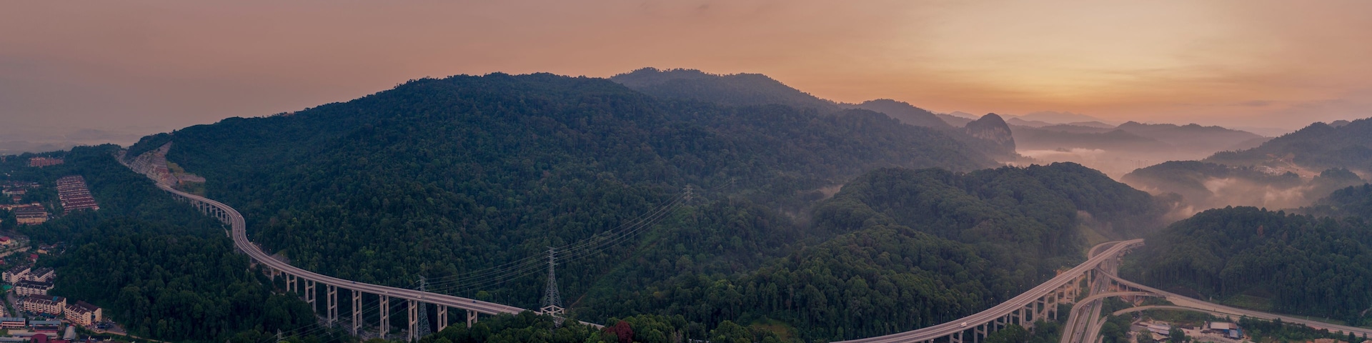 Uma longa ponte serpenteando por uma paisagem montanhosa com florestas densas.