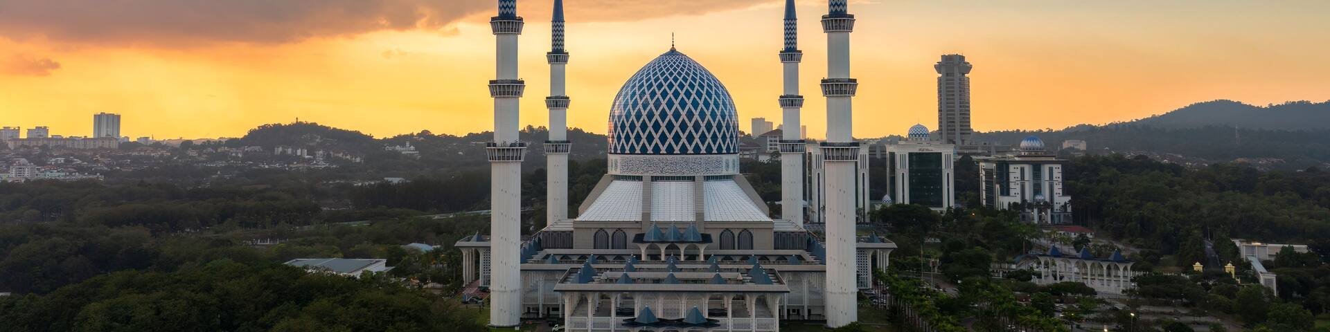 A mosque with a large central dome and four minarets, surrounded by trees and urban buildings.