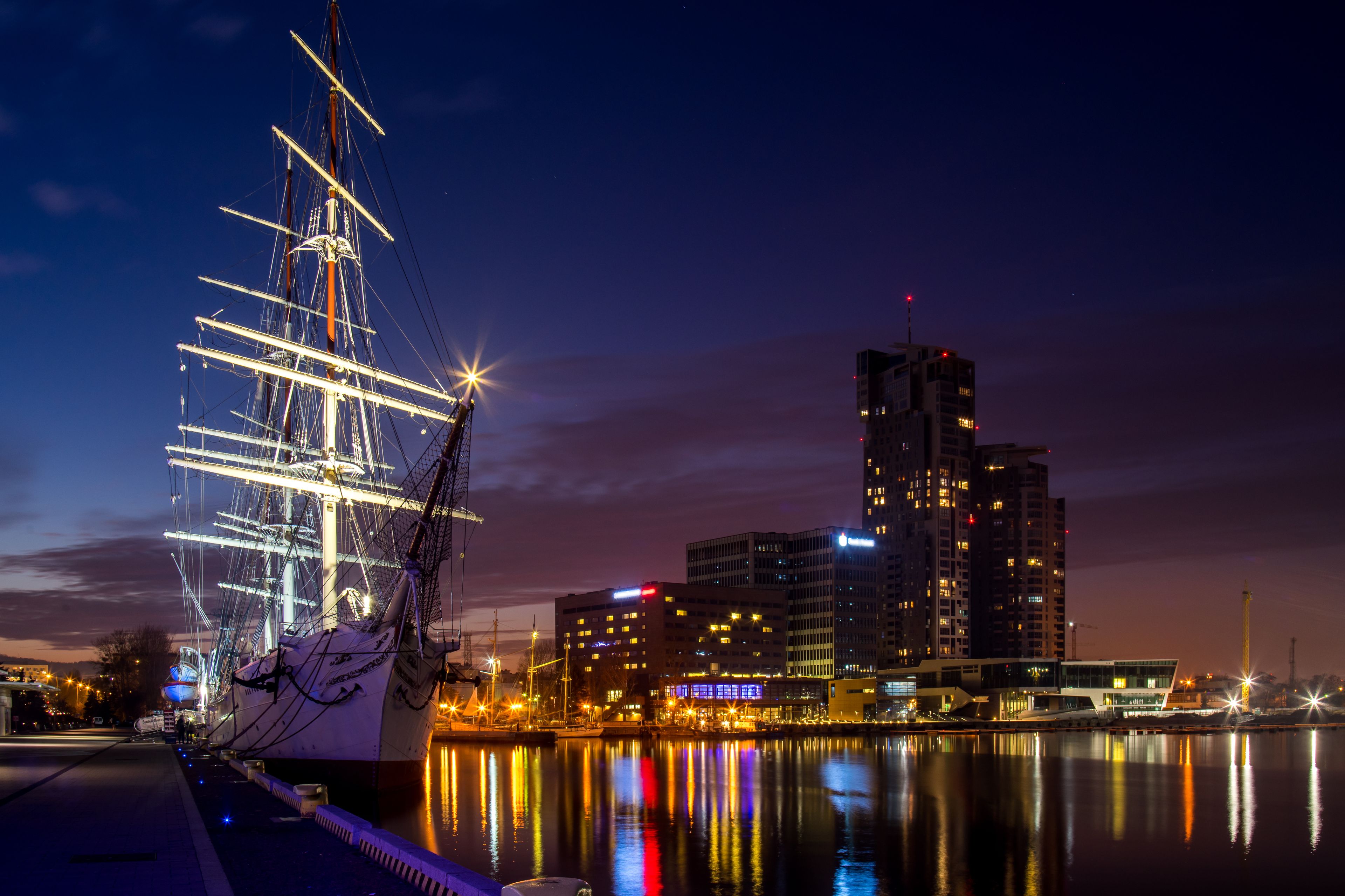 Un gran barco de vela amarrado en un puerto con edificios de la ciudad al fondo.