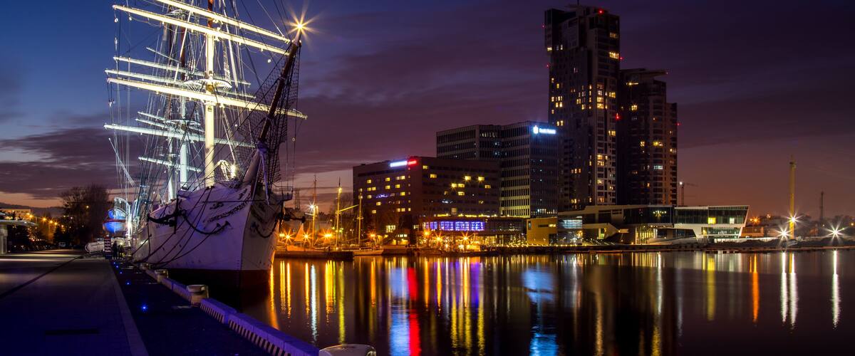 Ein großes Segelschiff liegt im Hafen vor städtischer Bebauung.