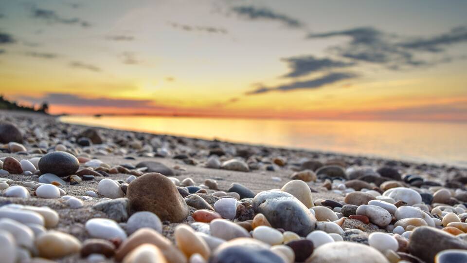 A pebble beach at sunset with a calm sea in the background.