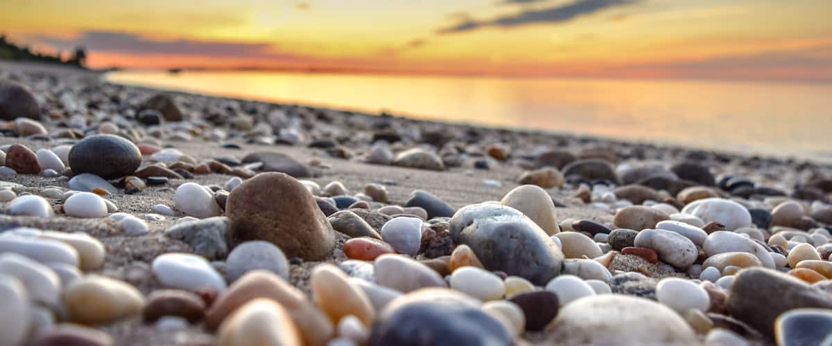 A pebble beach at sunset with a calm sea in the background.