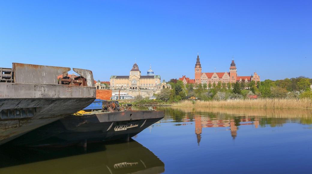 A river with a large ship docked on the left, a historic building with towers in the background, and a clear blue sky.