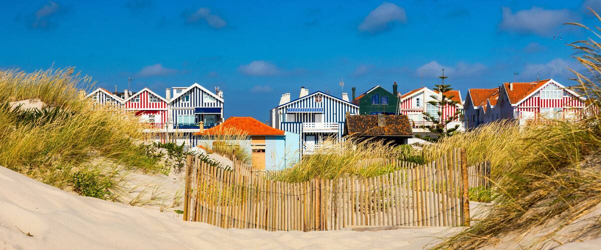 A row of colorful beach houses with sandy dunes and tall grass in the foreground.