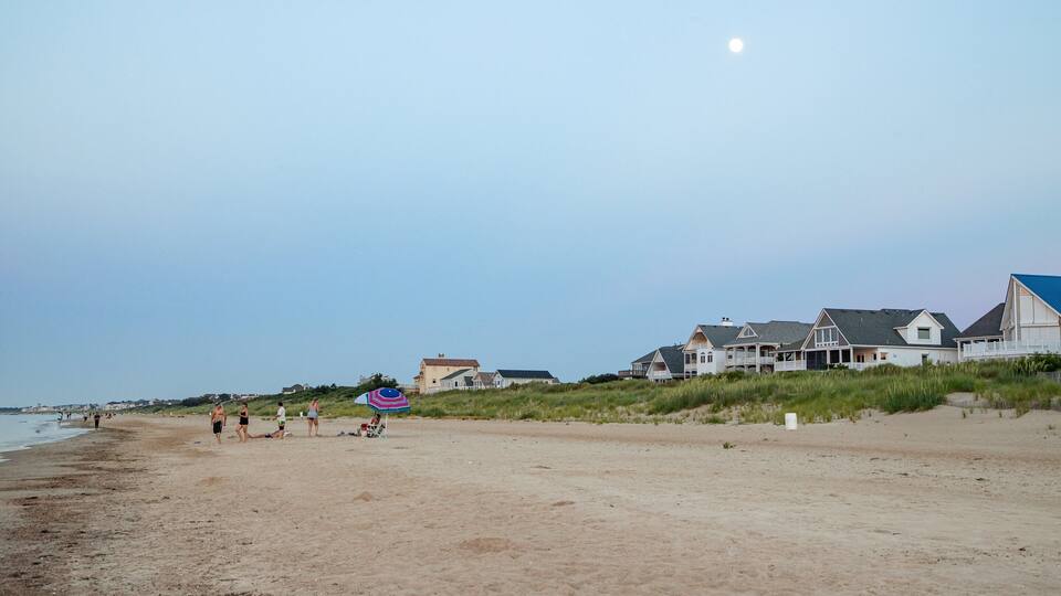 Une plage avec des gens, un parasol et des maisons en arrière-plan.