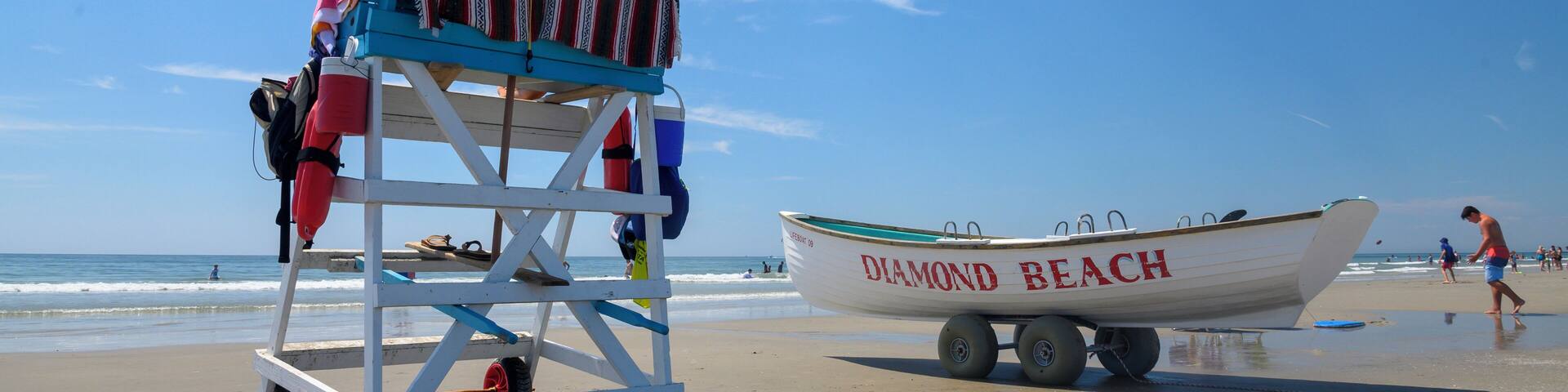 A lifeguard stand with an umbrella, a beach chair, and a boat labeled "DIAMOND BEACH" on the sand.