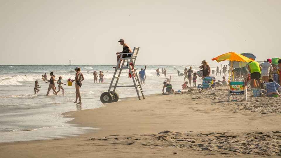 Una playa concurrida, gente, sillas de salvavidas y sombrillas.