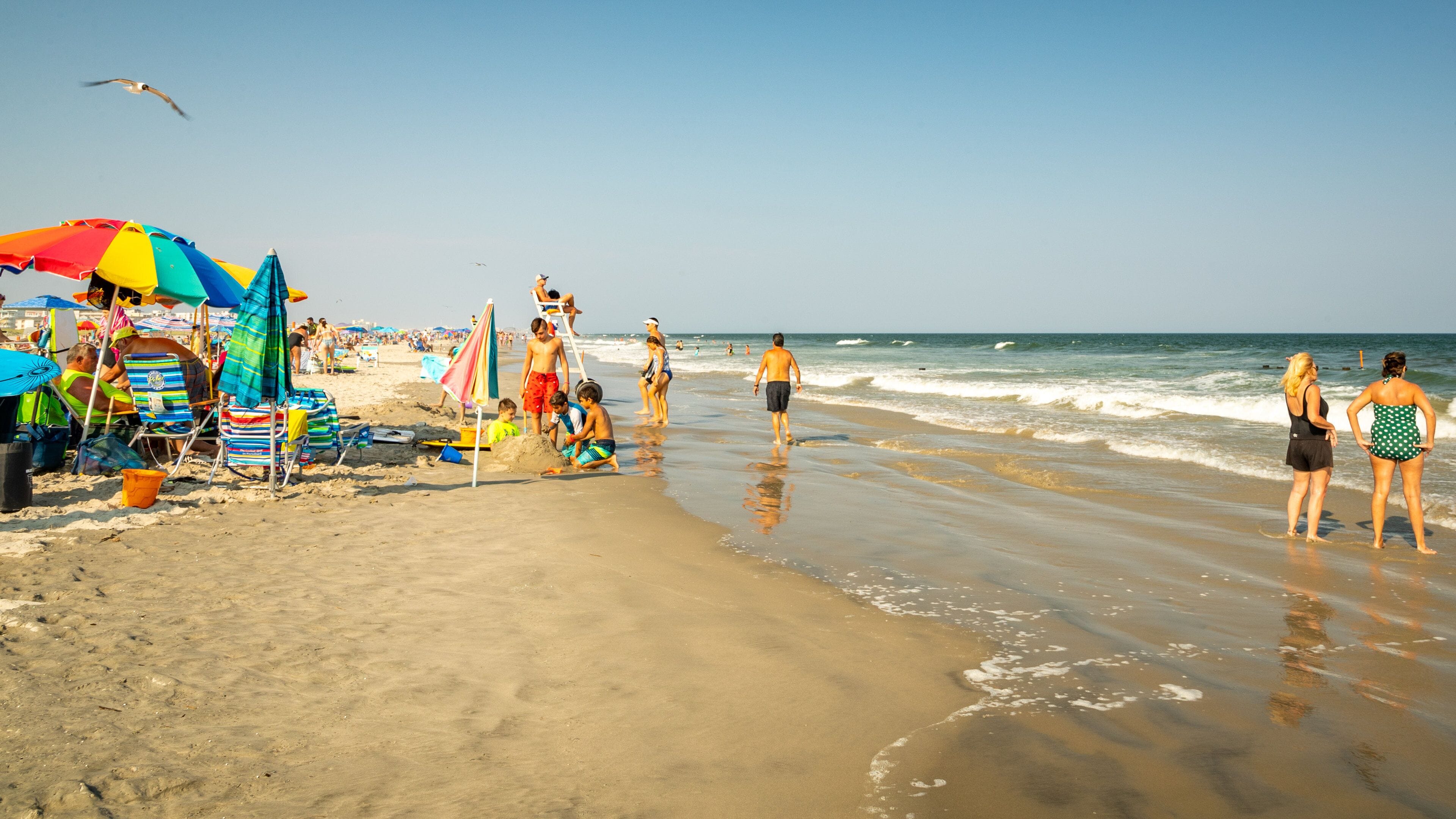 A crowded beach with colorful umbrellas, beach chairs, and people enjoying the sand and water.