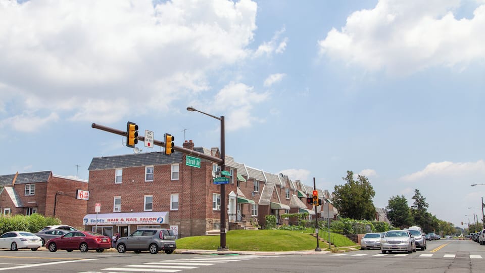A street intersection with traffic lights, cars, and a row of brick houses.