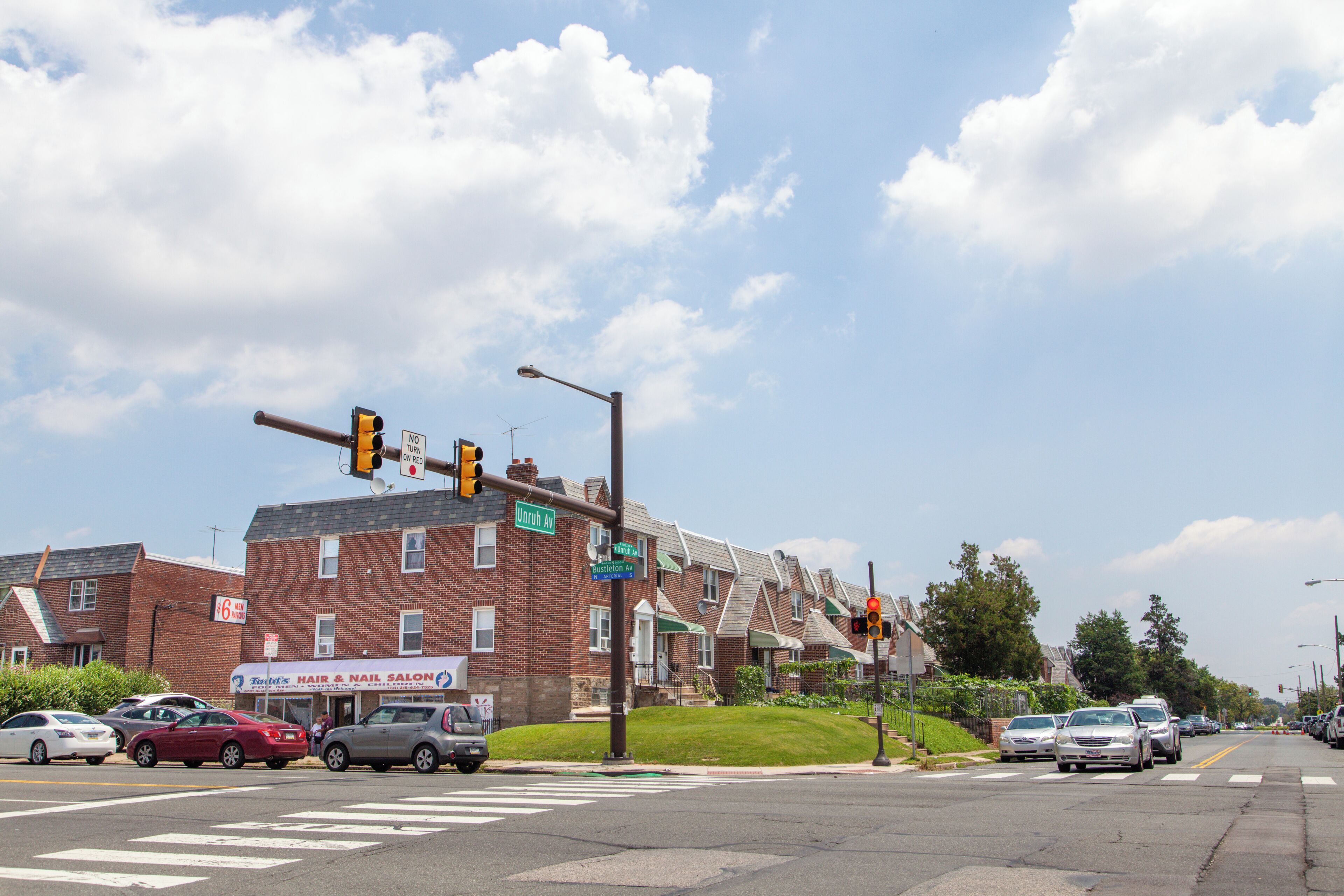 A street intersection with traffic lights, cars, and a row of brick houses.