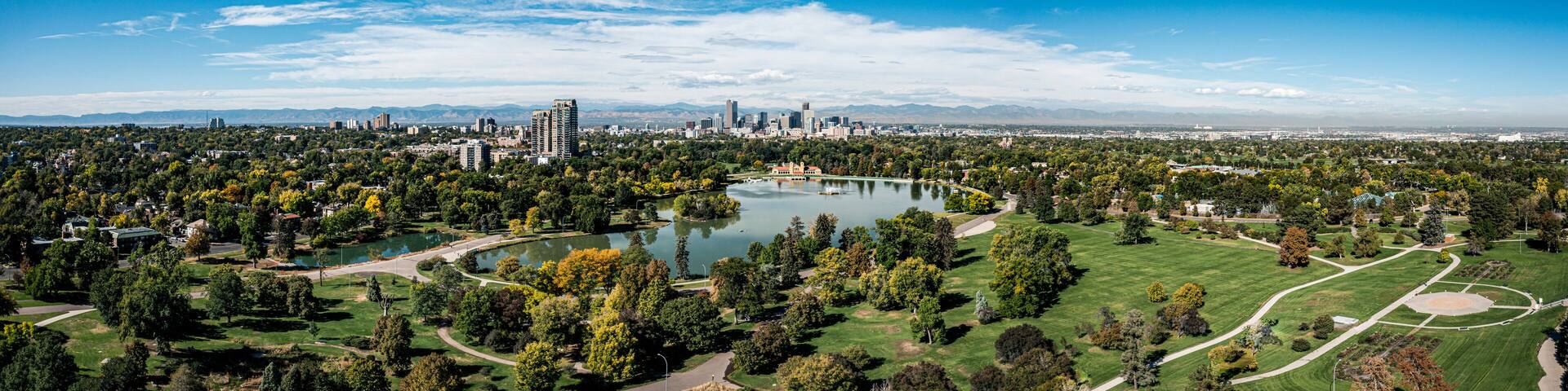 A cityscape with a large park featuring a lake, surrounded by greenery and urban buildings.