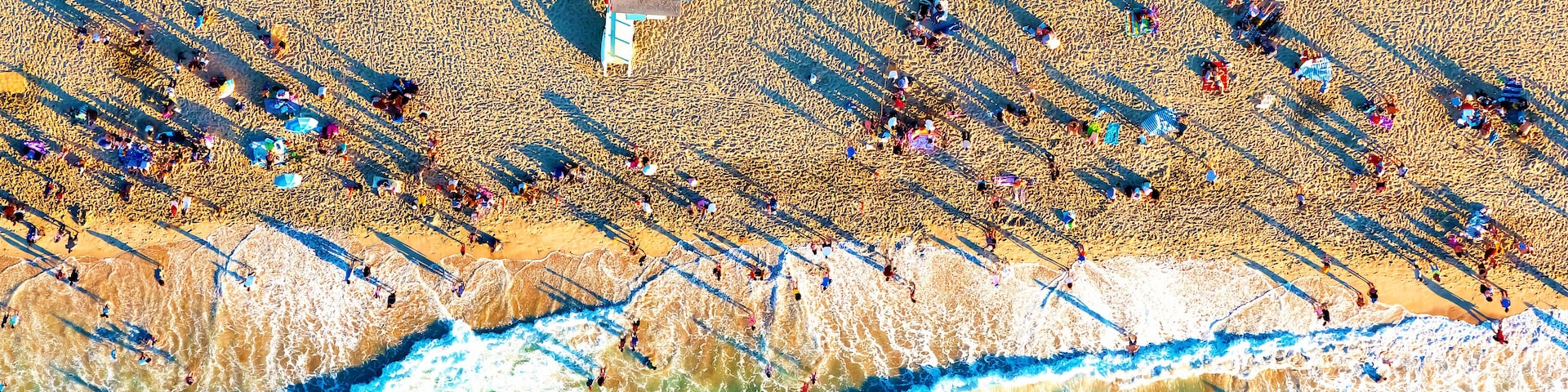 Ein überfüllter Strand mit Menschen und Sonnenschirmen, und Wellen schlagen an die Küste.