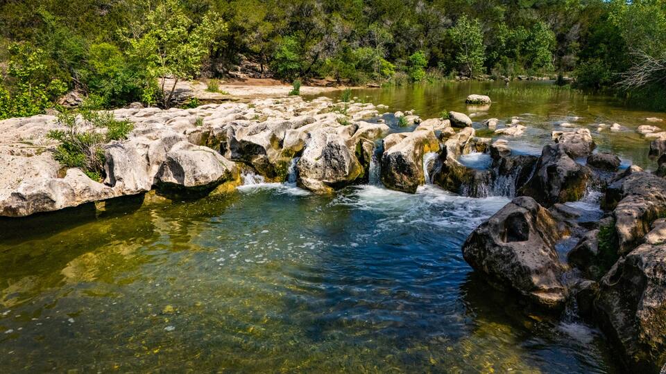 A clear stream with rocks and greenery.