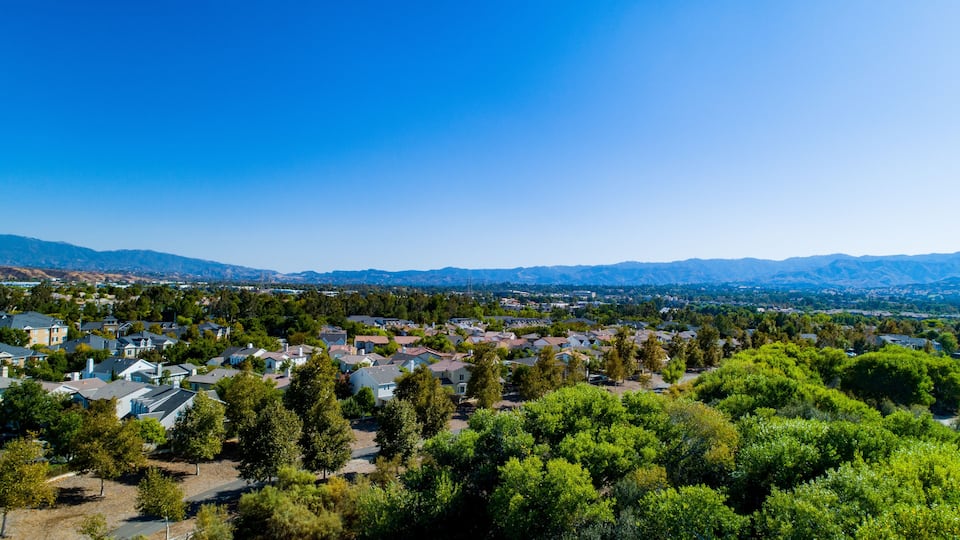 A residential area with houses, trees, and mountains in the background.