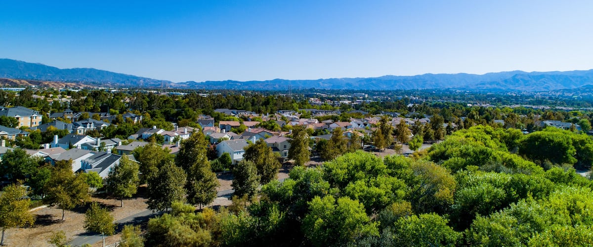 A residential area with houses, trees, and mountains in the background.