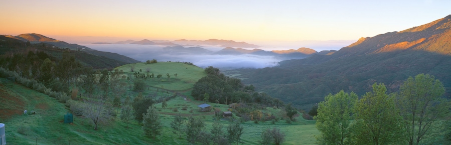 Un valle con colinas ondulantes, una casa pequeña y montañas al fondo.