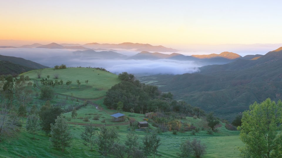 A valley with rolling hills, a small house, and distant mountains.