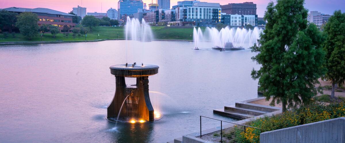 View of Omaha Nebraska skyline at sunset seen from Heartland of America Riverside Park with lake in view.