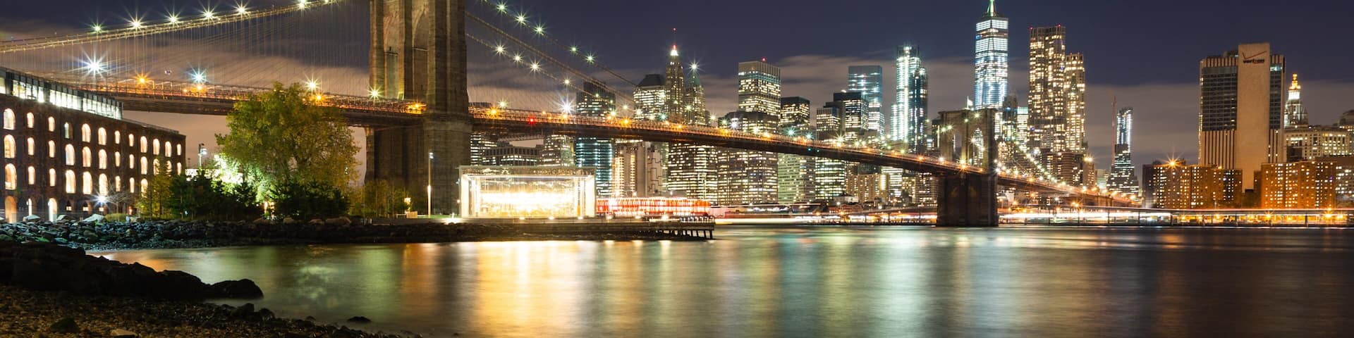 A nighttime cityscape with a prominent bridge and skyscrapers.