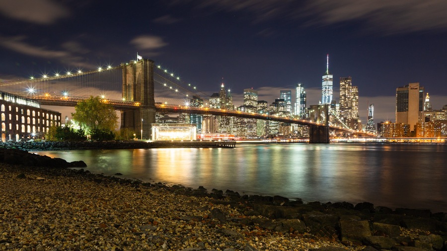A nighttime cityscape with a prominent bridge and skyscrapers.