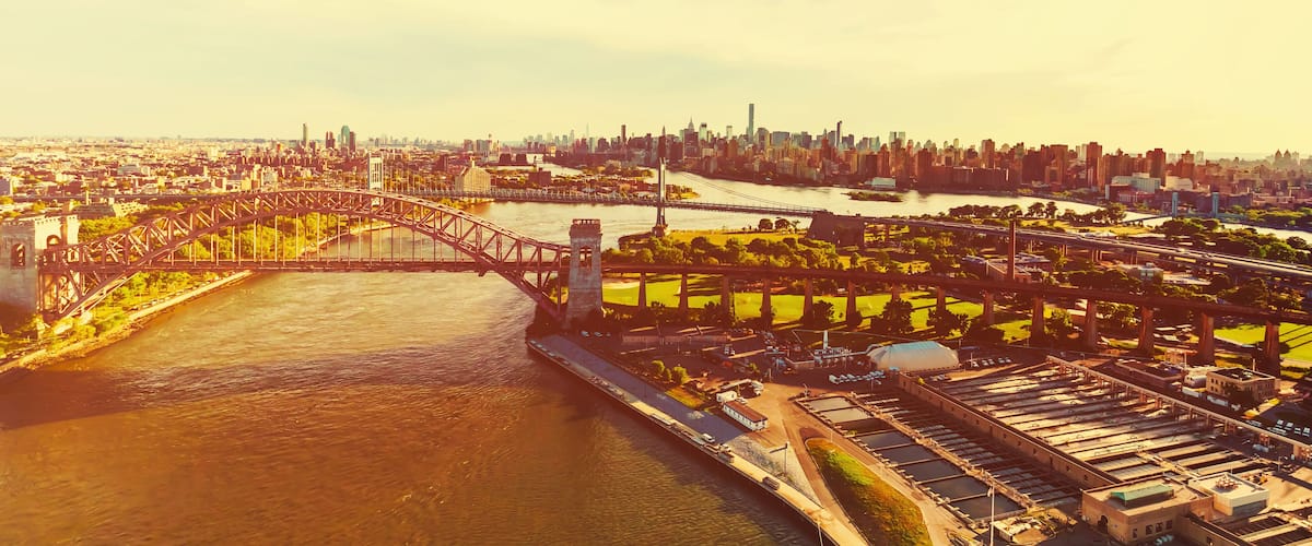 An aerial view of a city with a prominent bridge, a river, and a large industrial area with multiple buildings and parking lots.