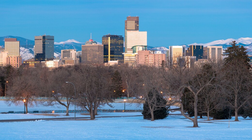 Golden Denver skyline at sunrise with snowcapped rockies in background and snow blanketed City Park and boat house in foreground