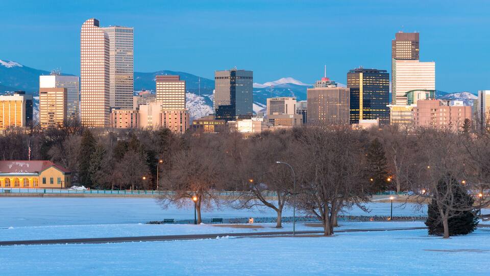 Golden Denver skyline at sunrise with snowcapped rockies in background and snow blanketed City Park and boat house in foreground