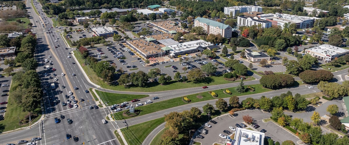 An aerial view of a city with a large parking lot, multiple buildings, and surrounding greenery.