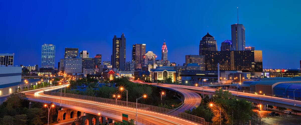 A city skyline at dusk with illuminated buildings and a curved highway.