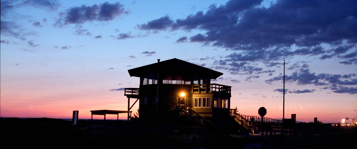 A lighthouse at sunset with a clear sky and a bench in the foreground.